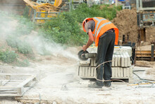 A Worker In Overalls Cuts A Piece Of Concrete Curb Using An Electric Grinder