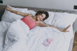 Calm young satisfied satisfied happy woman 20s wearing pajamas lying wrapped covered under blanket duvet on pillow with outstretched hands on bed rest relax at home Good mood morning bedtime concept