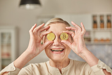 An elderly woman holds bitcoin coins in her hands near her eyes. Seniors retirement happy life concept