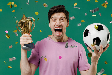 Young fun man fan wear basic pink t-shirt cheer up support football sport team hold in hand soccer ball cup champion win cup watch tv live stream scream isolated on dark green color background studio