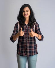 young girl showing thumb with the backpack on gray background