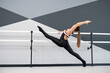 © serhiibobyk - Side view of gorgeous brunette woman stretching leg on handrail, doing split. Fit flexible female athlete wearing sports outfit practicing in dance studio, hi tech interior. Concept of gymnastics.