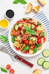 Wall Mural - Panzanella - Italian salad from vegetables and bread. Salad with tomatoes, onions, cucumbers, bread, capers and basil in a white plate on a gray concrete background. Vegan salad, Italian cuisine