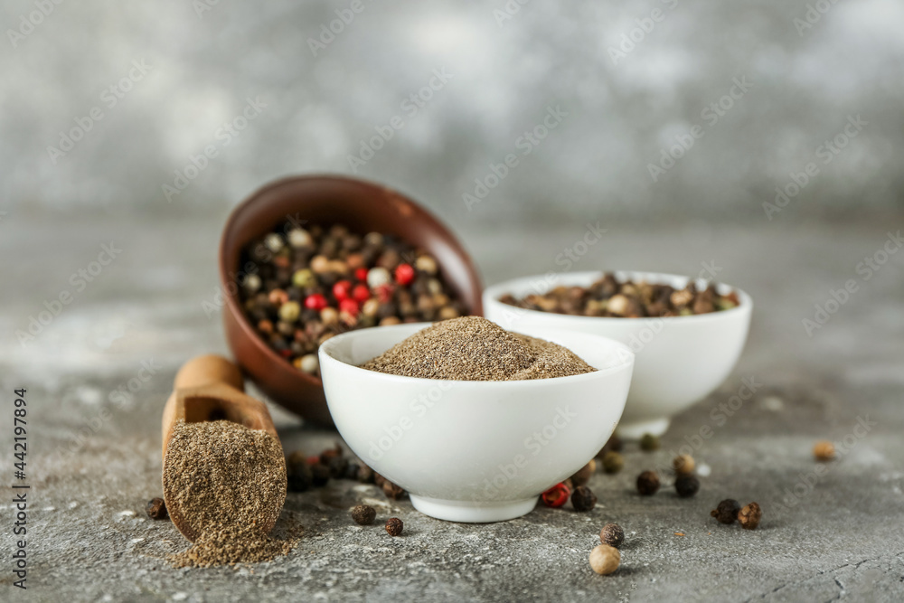 Bowls with black pepper powder and peppercorns on grunge background