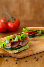 two tasty sandwiches with ham, green salad, cucumbers and tomatoes on the wooden background.toasted homemade sandwich with fresh vegetables on the brown cutting board.vertical.copy space