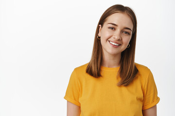 Wall Mural - Portrait of candid young woman smiling white teeth, tilt head friendly and looking happy at camera, wearing yellow t-shirt against white background