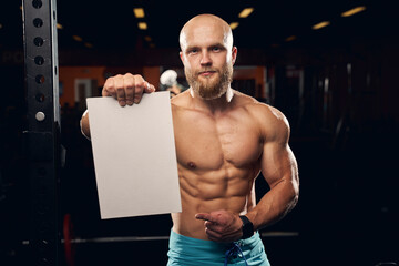 Wall Mural - Shirtless athletic man holding a blank board at the gym