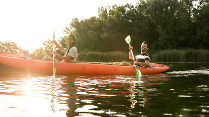 Wall Mural - Smiling young couple kayaking in a river surrounded by the beautiful nature on a summer day