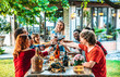 © Davide Angelini - Group of friends having fun at bbq dinner outdoor in garden restaurant - Multiracial people toasting red wine glasses at barbecue backyard home party - Friendship, youth and party concept