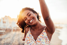 Cheerful Woman Smiling At The Beach On Sunset - Happy African Female Having Fun Walking By The Sea - People And Happiness Concept	
