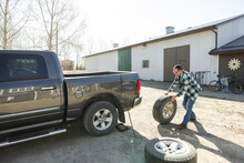 Man Rolling Tire At Rear Of Pickup Truck