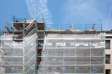 Front exterior view of net wrap scaffolding in front of building at construction site.