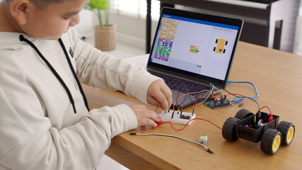 Young asia student remotely learn online at home in coding robot car and electronic board cable in STEM, STEAM, mathematics engineering science technology computer code in robotics for kids concept.