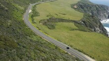 Drone Reveal Car Driving On Big Sur Highway Behind Green Hills On California Coast