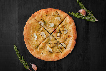 Sliced focaccia with garlic and rosemary on black background