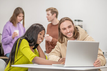 Wall Mural - Darkskinned girl and caucasian guy interestedly looking at laptop