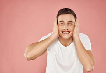 Wall Mural - cheerful man gesturing with his hands in a white t-shirt on a pink background