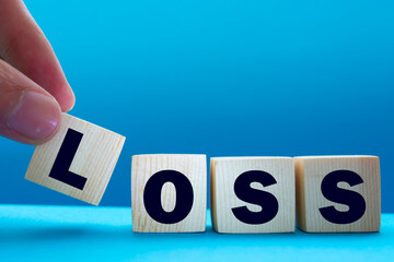 Canvas Print - A businessman holds wooden cubes with a word LOSS on a blue background, with space to copy the text, business concept