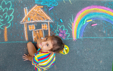 Wall Mural - The child draws a house and a rainbow on the asphalt with chalk. Selective focus.