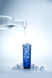 Pure water is poured from a transparent bottle into a blue glass with ice cubes.
