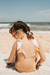 Portrait six year girl in yellow swimsuit wearinmg sunglasses on the beach. hot summer day.