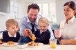 © Monkey Business - Children Wearing School Uniform In Kitchen Eating Breakfast Waffles As Parents Get Ready For Work
