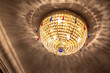 Wonderful round glowing luster with shiny glass beads on white ceiling with shadows patterns in theater hall low angle shot