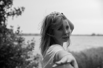 Young beautiful girl with long hair in white coat on sunny day stretches her hand forward. Hand out of focus. Trying to touch the camera. Black and white image.