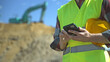 © M-Production - Builder with hard hat and high vis jacket using smartphone. Close-up.