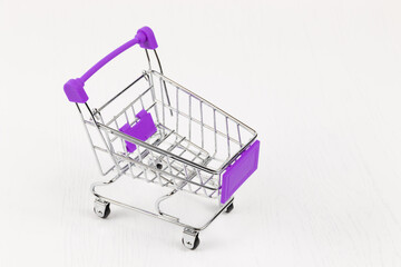 Wall Mural - empty metal shiny grocery cart on wheels on white wooden table background