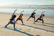© Wavebreak Media - Diverse group of women practicing yoga, standing stretching at the beach