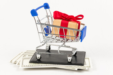 Wall Mural - metal chrome shiny shopping trolley on wheels with gift box on wallet with dollars on white background. selective focus