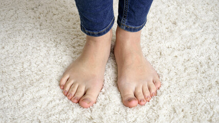 Closeup of barefoot woman in jeans standing on soft white carpet and moving toes