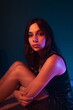 © ADDICTIVE STOCK - Young woman sitting in neon illumination