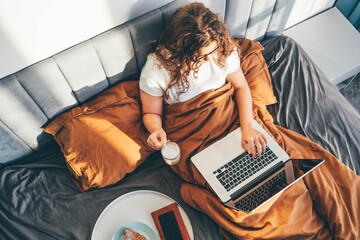 Woman sitting on bed and drinking coffee at the sunny morning bedroom. 