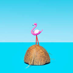 A flamingo toy standing on half of coconut with blue sea and blue sky background. Tropical isolated lovely Island concept.