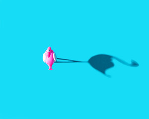 A flamingo toy standing on blue background with sun shadow a side. Drone shoot concept, flat lay.