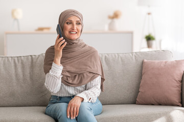 Wall Mural - Happy Senior Female In Hijab Talking On Cellphone Sitting Indoor