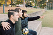 © Austockphoto - Side view photo of 3 smiling interracial man sitting on a field, one is pointing a finger