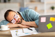 Lazy unproductive young guy wearing funny sticky notes with open eyes on his glasses, sleeping at workplace