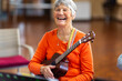© Austockphoto - elderly woman holding ukulele and laughing