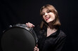 portrait of a smiling young beautiful drummer girl, in black, holding a snare drum, posing. On a black background