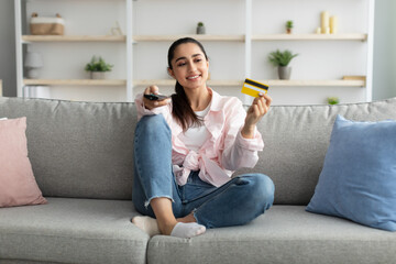 Wall Mural - Female relaxing on couch, holding remote controller and credit card