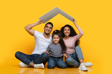 Poster - Family Housing. Happy Arab Family Of Three Sitting Under Carton Roof