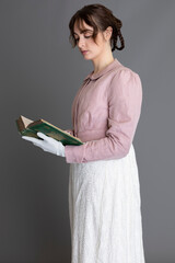 A young Regency woman wearing a cream embroidered dress and pink linen spencer