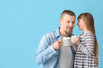 Wall Mural - Happy daughter and father with cups of hot cocoa on color background