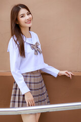 Cute and young girl wearing Japanese, Korean style schoolgirl uniform and pose to camera with fun and happy in front of school building