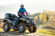 Happy active female driver in protective helmet enjoying extreme riding on ATV quad motorbike in fall mountains at sunset.