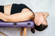McKenzie method exercise to relieve neck pain, a woman lying on the massage table and lowering her head toward the floor while doing neck pain relief exercises