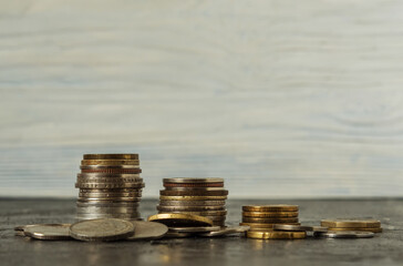 On a black background, there are four stacks of coins in descending order. Coins are scattered in the foreground. Business planning, finance and savings concept.